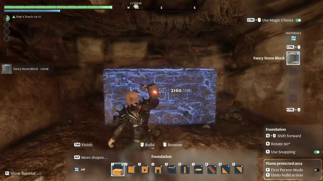 Character using a tool on a glowing blue foundation block in a cave-like environment.